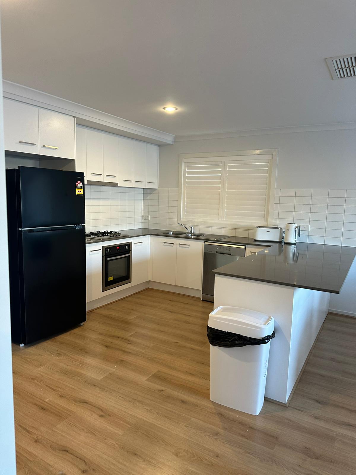 Picture of the kitchen amenities in an SIL house. There is a black fridge, an island with white cupboards, a cooker and dishwasher.