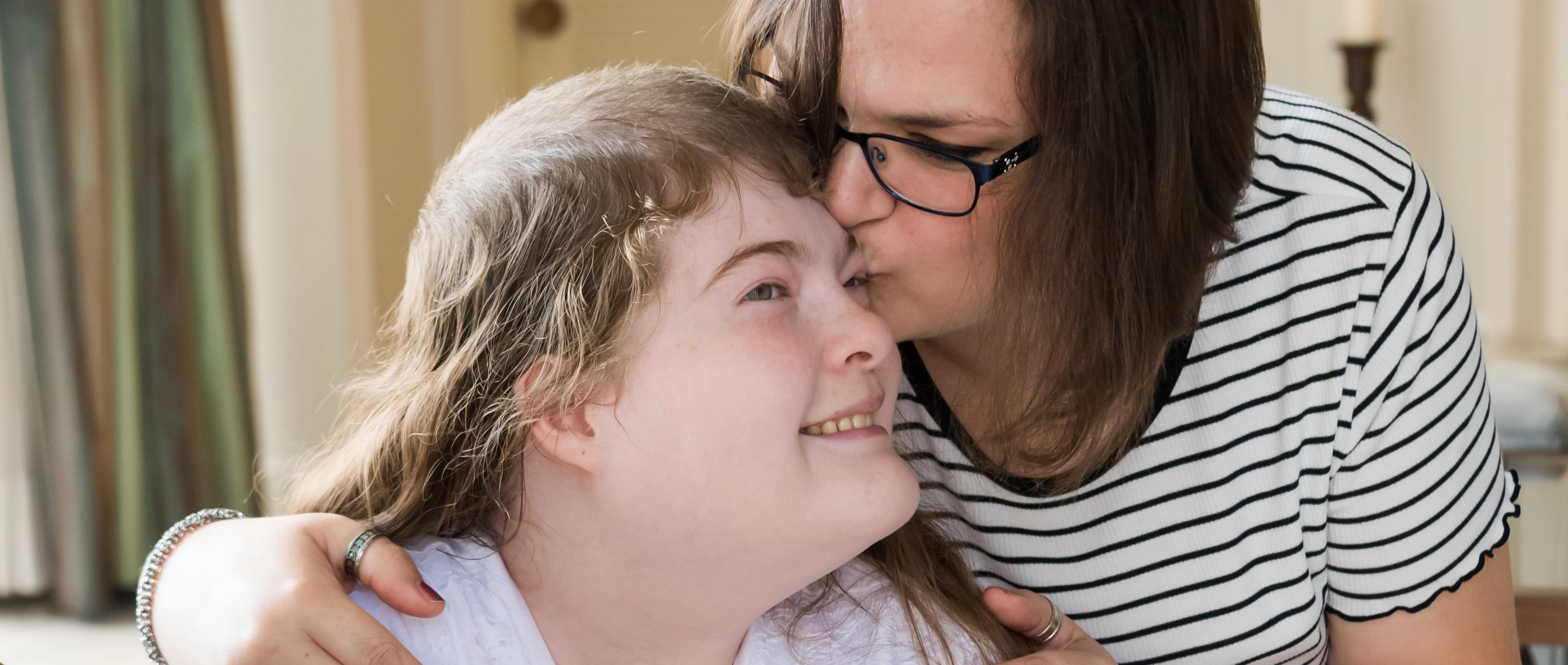 A female care assistant kissing a young girl with prader-willi-syndrome on the forehead