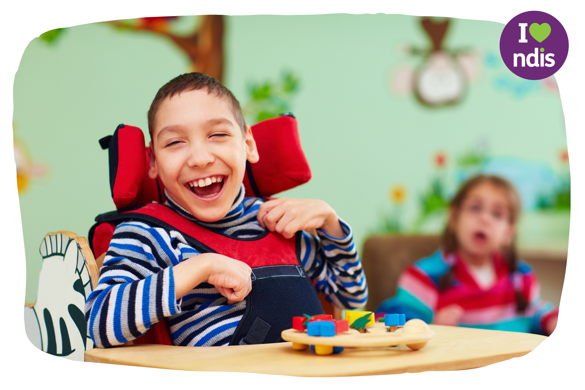 A young boy with a disability who is in a high chair laughing with toys in the table in front of him