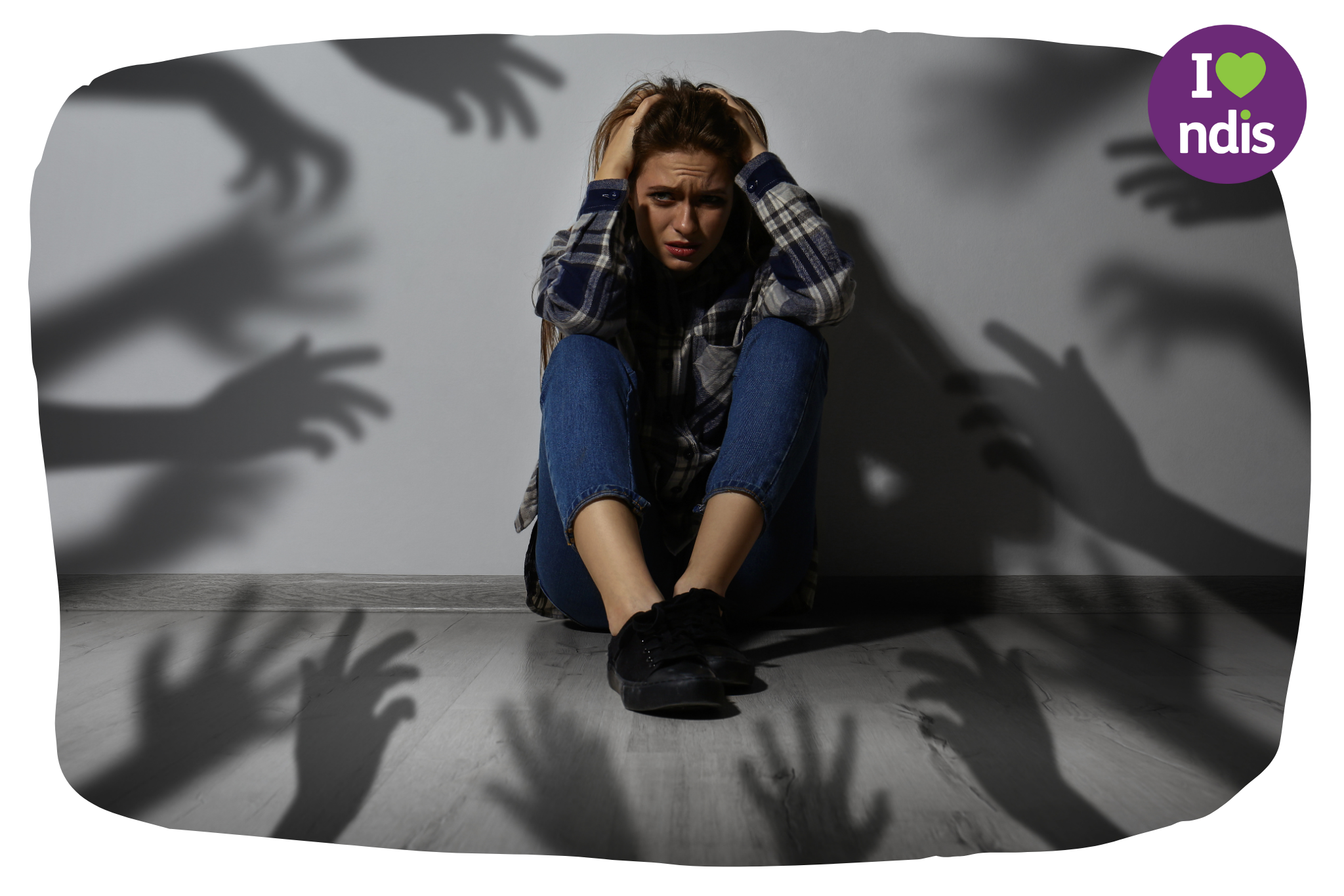 A woman sits on the floor in a dark room holding her head in fear. Shadows on the wall behind her suggest there are people trying to put their hands on her.